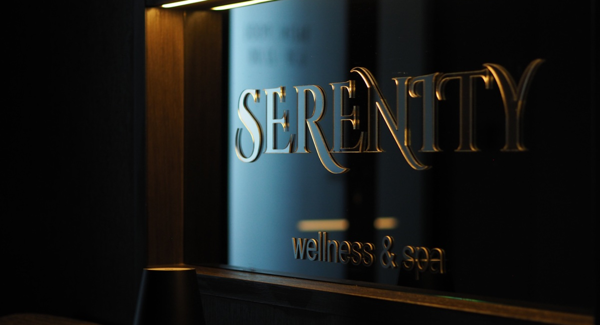 Napis z zlatimi crkami 'Serenity Wellness & Spa' na crni podlagi.