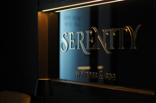 Napis z zlatimi crkami 'Serenity Wellness & Spa' na crni podlagi.