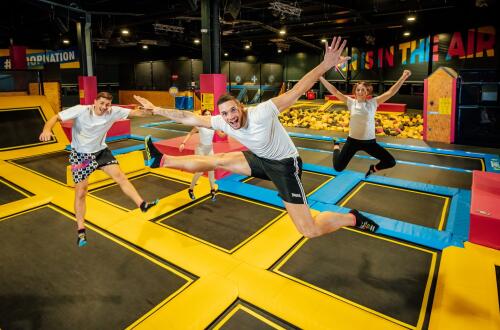 A group of people jumping on trampolines in a colourful indoor sports and entertainment park.