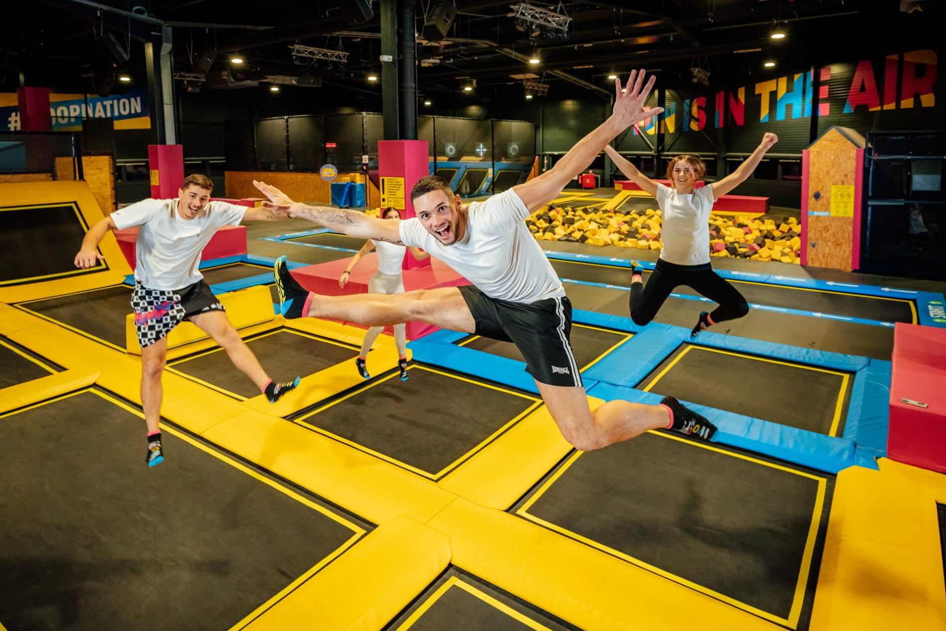 A group of people jumping on trampolines in a colourful indoor sports and entertainment park.