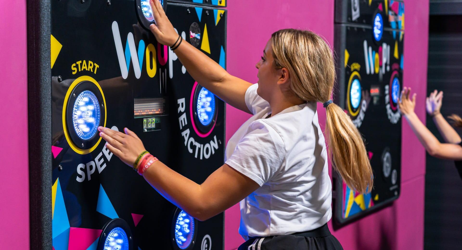 A person pressing illuminated buttons on an interactive reaction wall during a speed game.