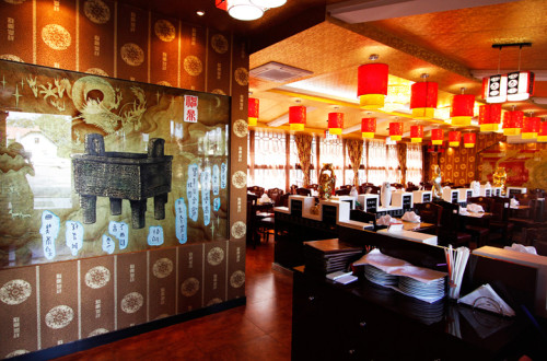 Tradicionalna kitajska slika na zidu. V ozadju restavracija z mizami in stoli.
