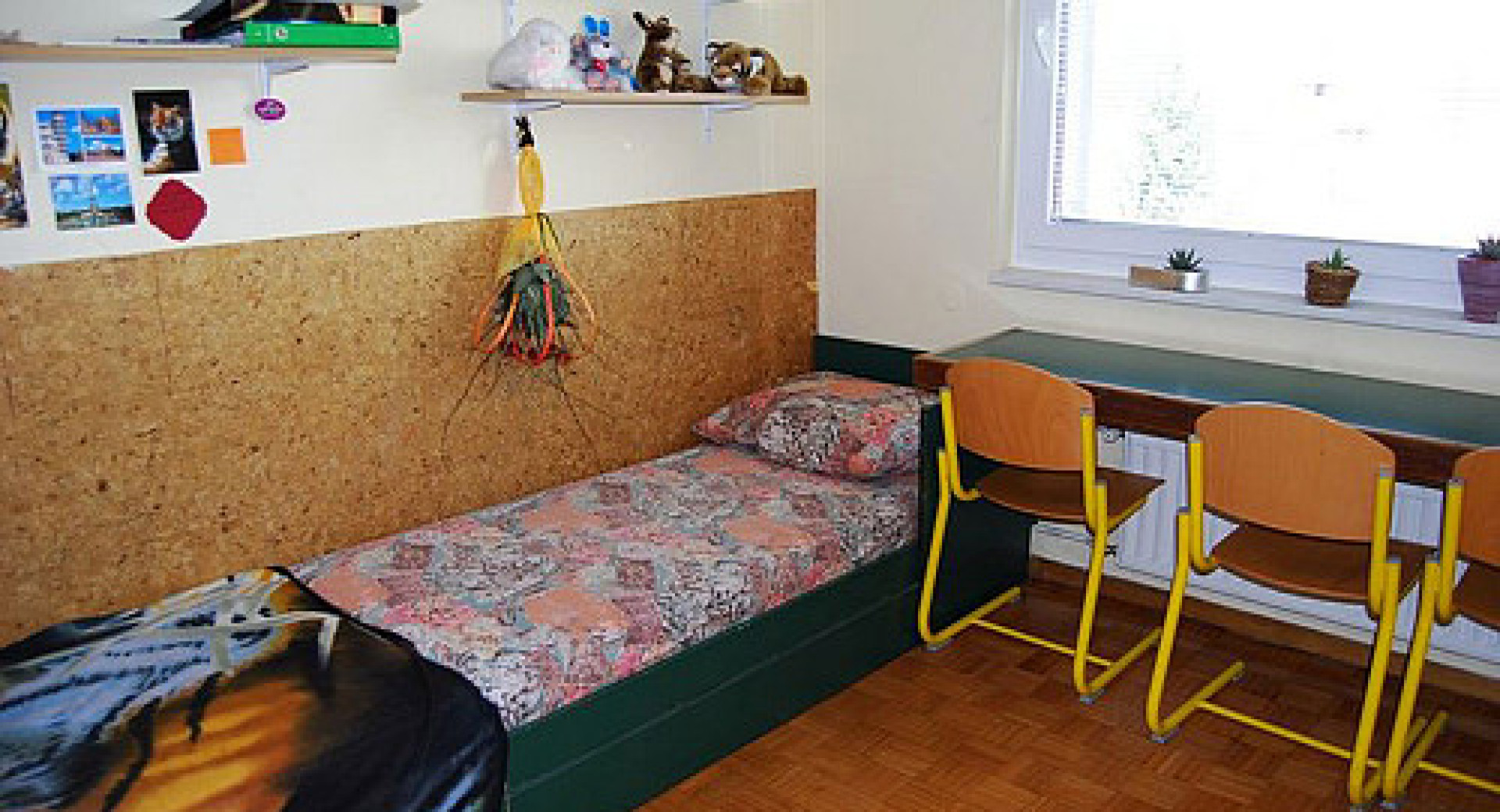 Postelja in pisalna miza v sobi dijaškega doma.