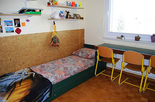 Postelja in pisalna miza v sobi dijaškega doma.