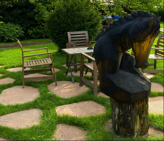 Lesena miza in stoli v parku gostilnice. Pred njimi lesena rezbarija konjske glave.