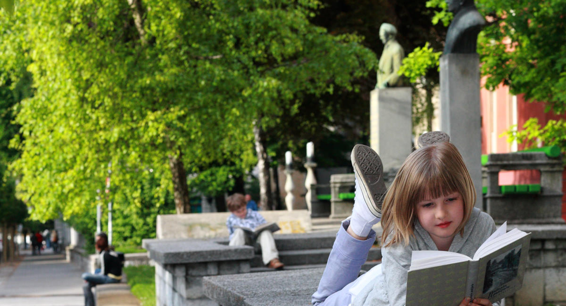Otroka bereta knjigo v zelenem parku v Ljubljani.