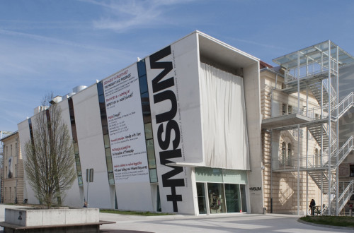 The exterior of a white building with the sign "+MSUM."