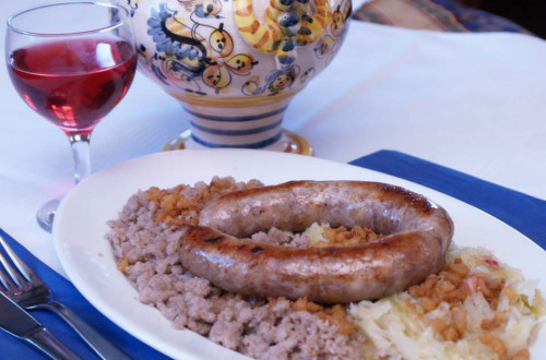 Pečenica, s kislim zeljem in ajdovo kašo. V ozadju majolka in kozarec vina. 