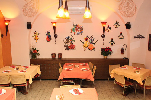 Notranjost restavracije z mizami in stoli, ter indijskimi simboli. 