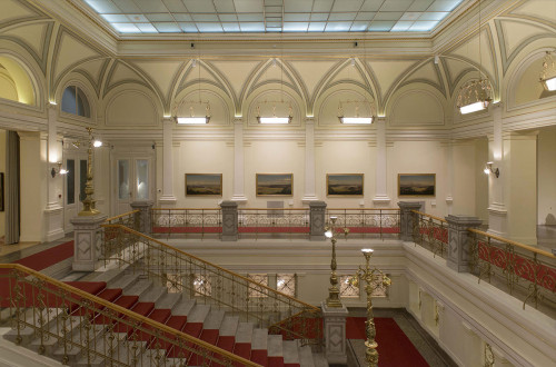 Mogočno stopnišče galerije. V ozadju razstavljene slike na zidu.