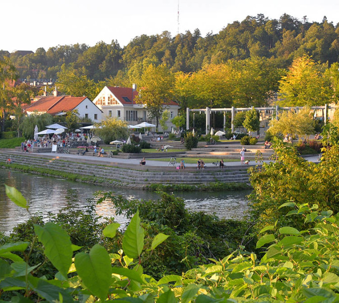 Ljudje na Špici, reka Ljubljanica in zelenje.