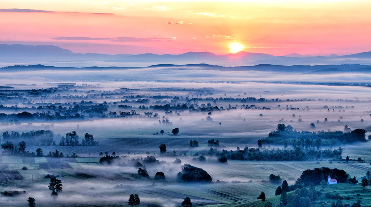 Sunrise over a plain with mist. A plain with trees and meadows in the fog.