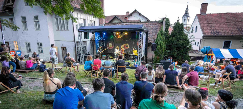 Ljudje sedijo na travi ter gledajo in poslusajo koncert.