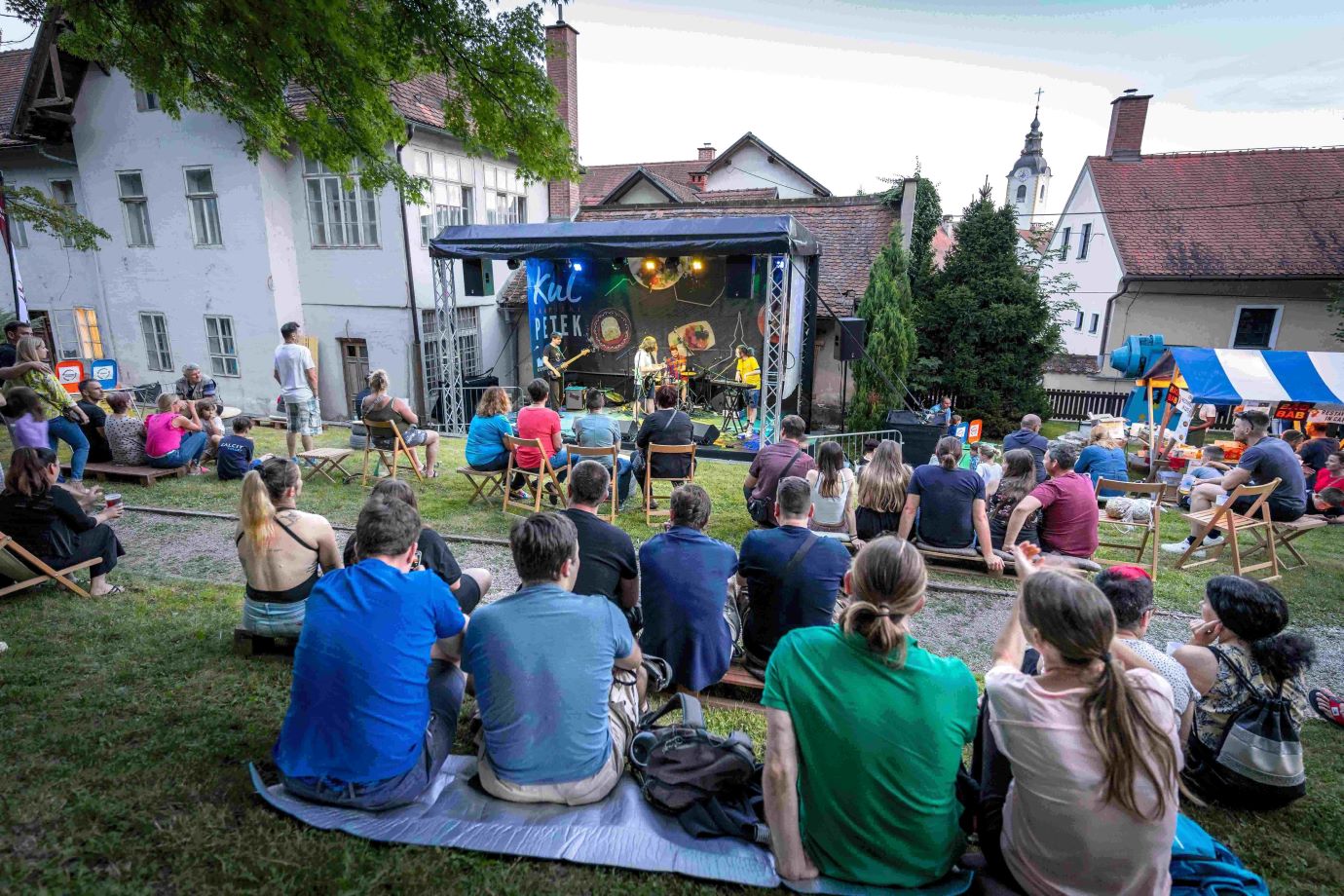 Ljudje sedijo na travi ter gledajo in poslusajo koncert.