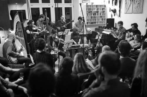 Crno-bela fotografija orkestra, ki igra v mali sobi.
