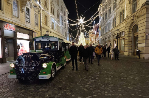 A city train in black and green stands in a festive town decorated with lights.