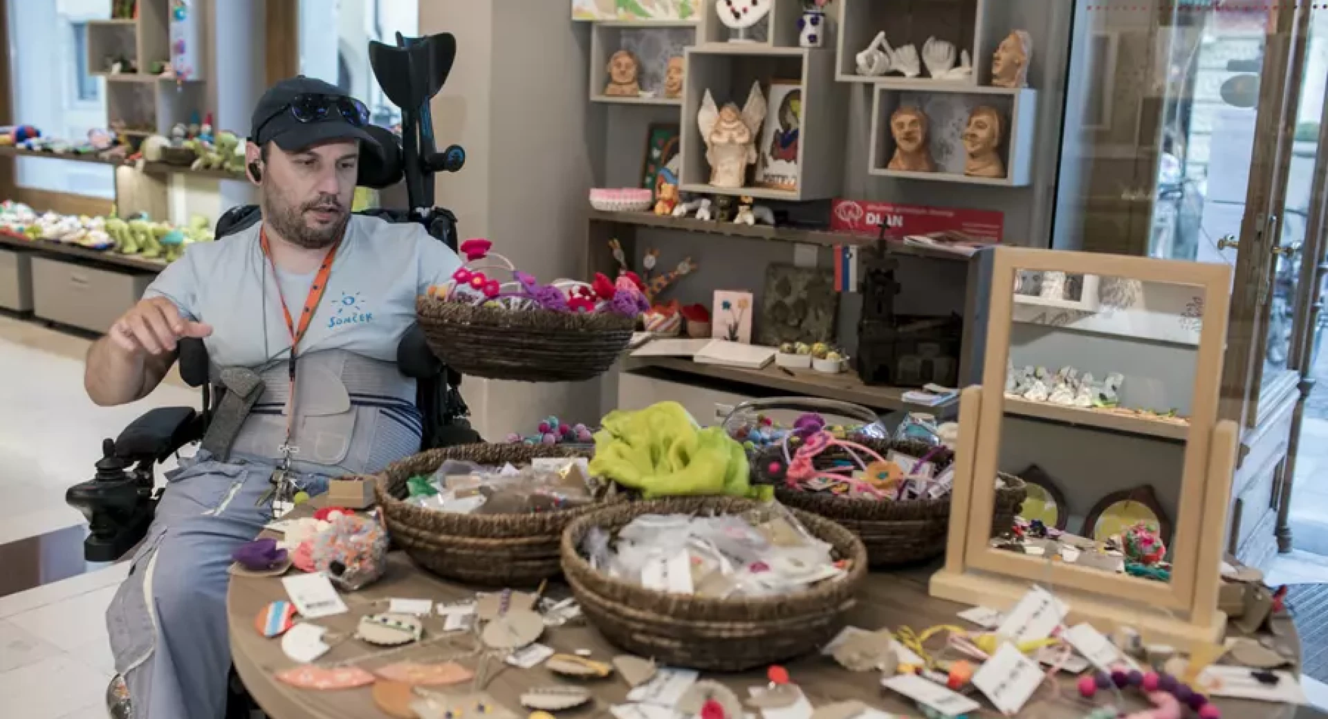 A man in a wheelchair with products placed in front of him on a table in the store.