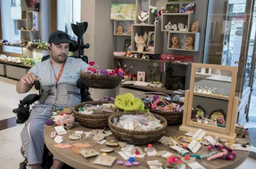 A man in a wheelchair with products placed in front of him on a table in the store.