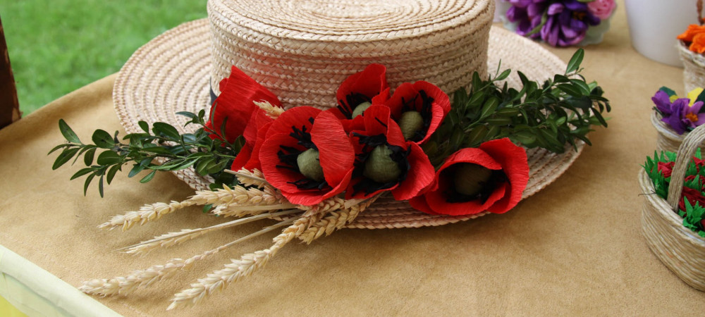 A straw hat decorated with greenery, red poppy flowers, and wheat.