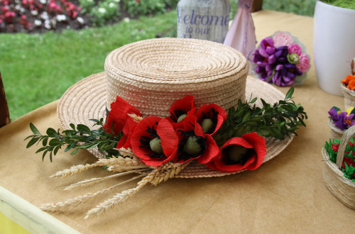 A straw hat decorated with greenery, red poppy flowers, and wheat.