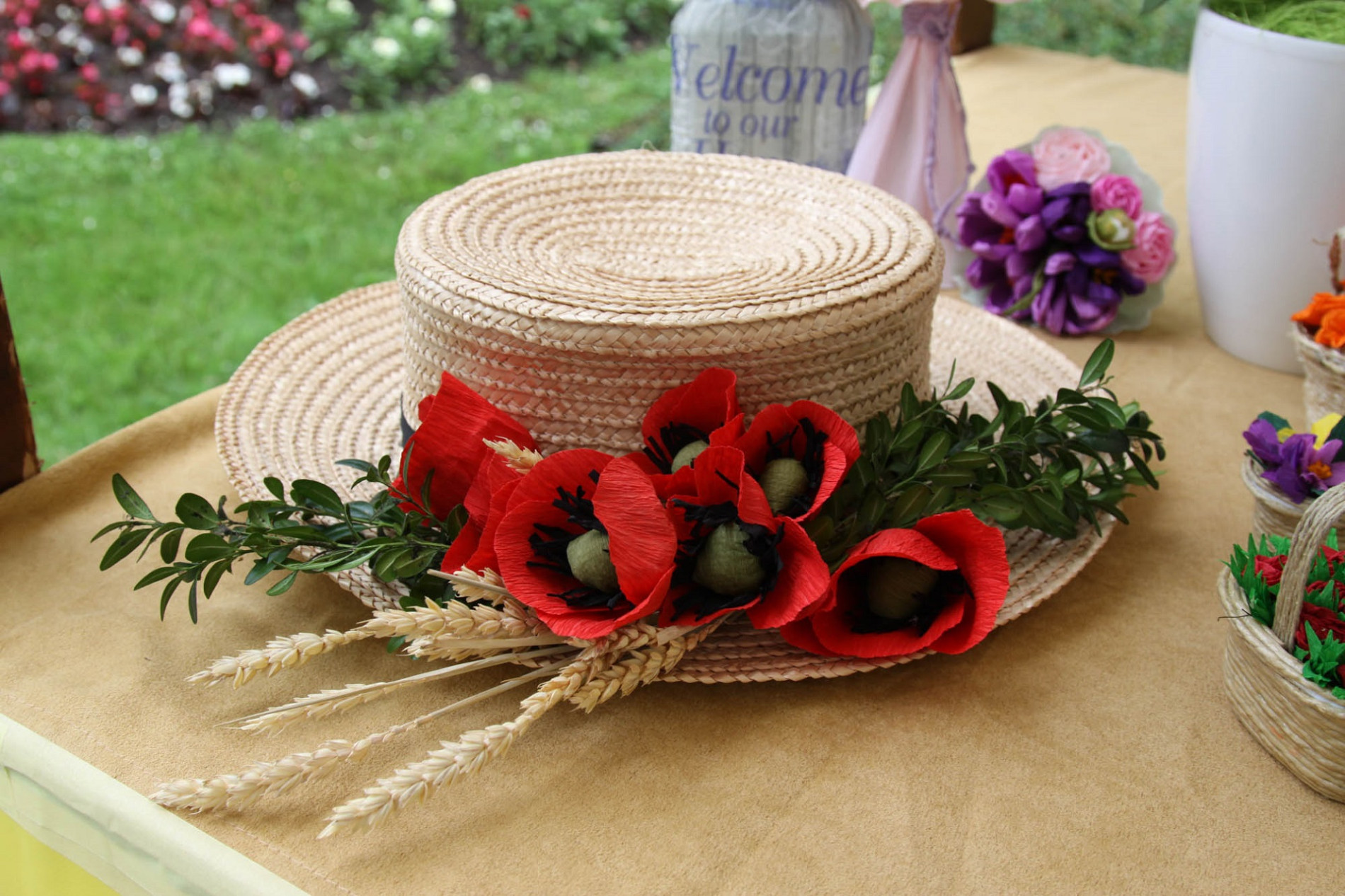 A straw hat decorated with greenery, red poppy flowers, and wheat.