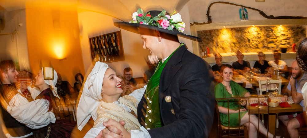 Par v narodnih nosah plese v objemu in se smeji.