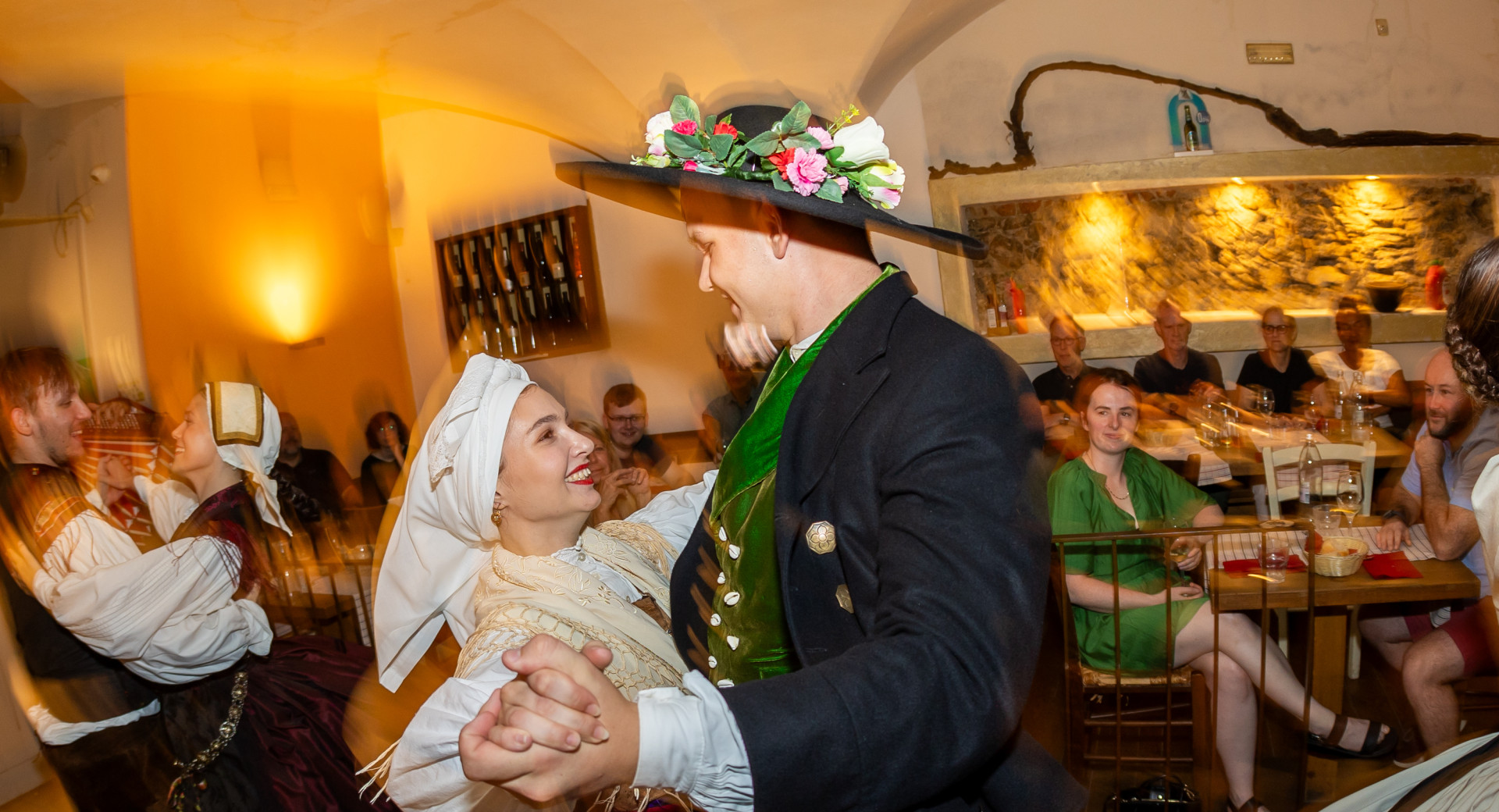 A couple in traditional folk costumes dances in an embrace and laughs.