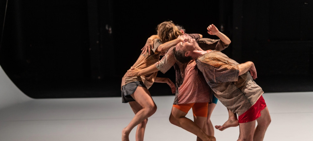 Four dancers are performing contemporary dance on a grey stage with a black background.