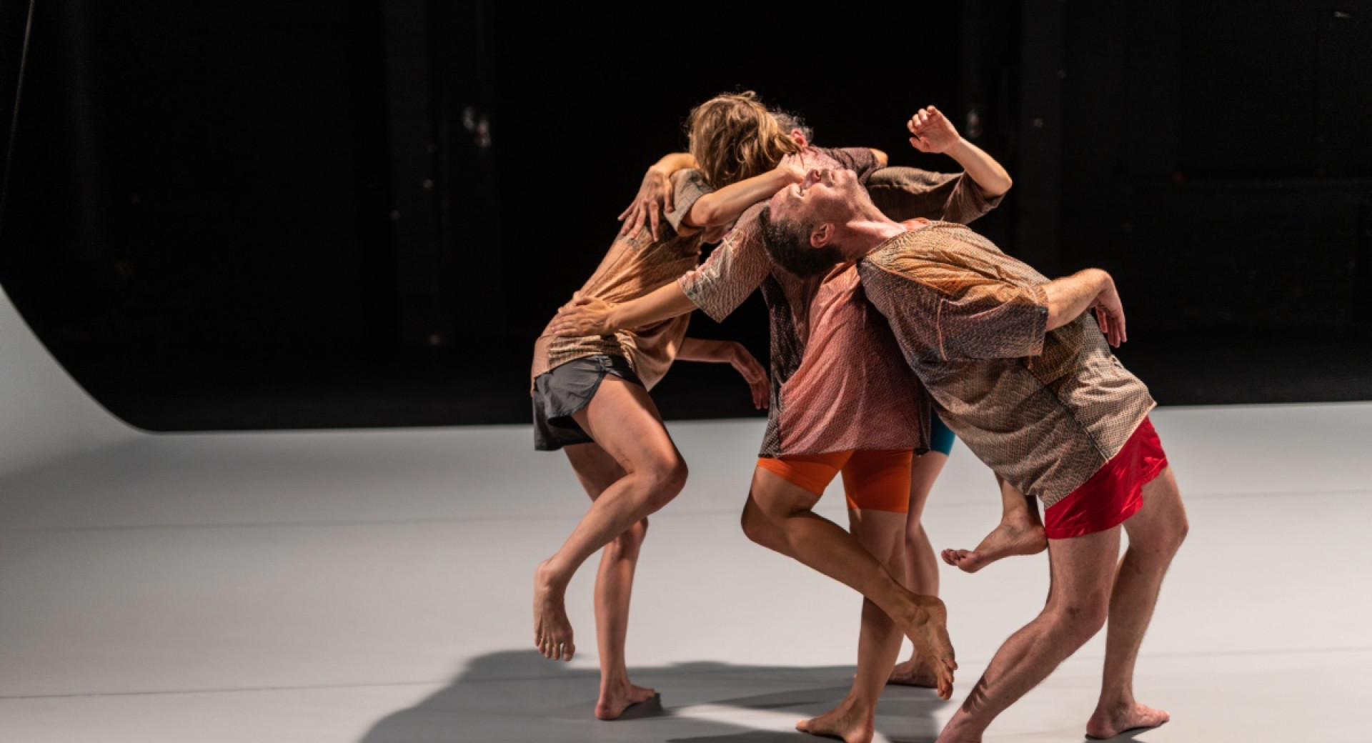 Four dancers are performing contemporary dance on a grey stage with a black background.