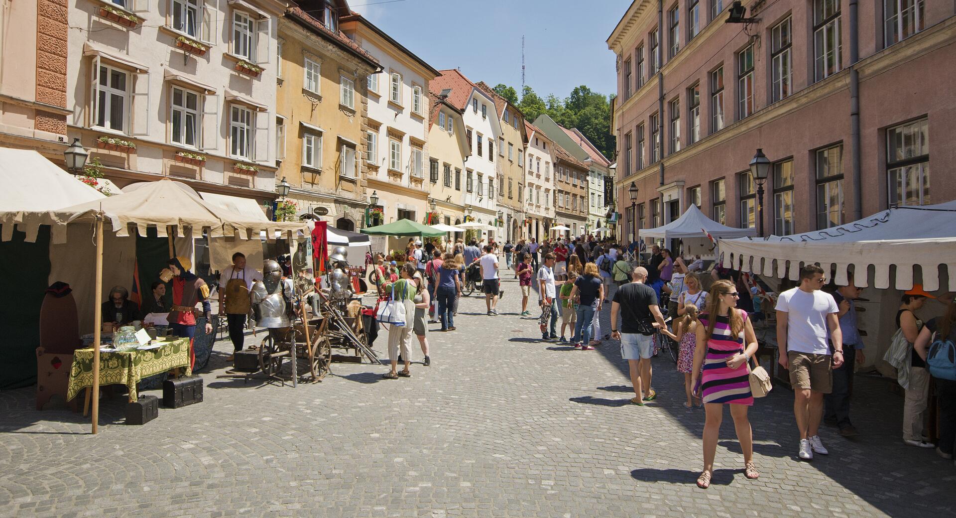 Ljudje se sprehajajo na ulici med stojnicami v starem delu mesta.