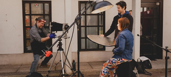 Zenska pod lucjo, moski snemalec in drug moski med scensko postavitvijo.