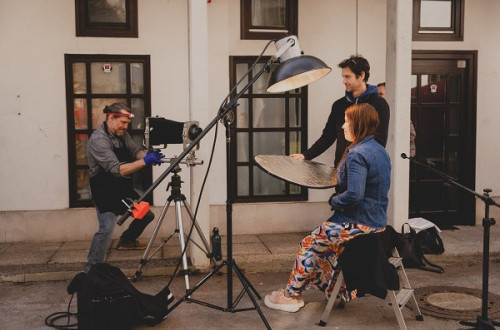 Zenska pod lucjo, moski snemalec in drug moski med scensko postavitvijo.