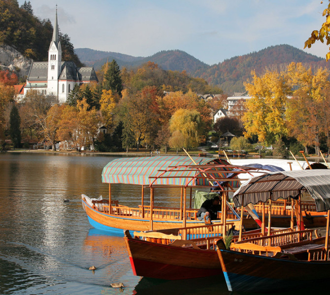 Une barque en bois sur le lac, une église en arrière-plan. Couleurs d'automne.