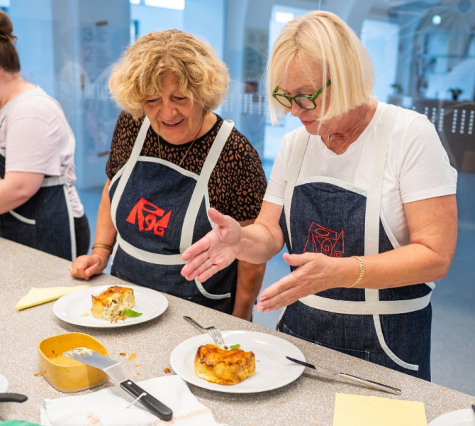 Dve zenski s svetlimi lasmi gledata peceno slano pito in se pogovarjata o njej.