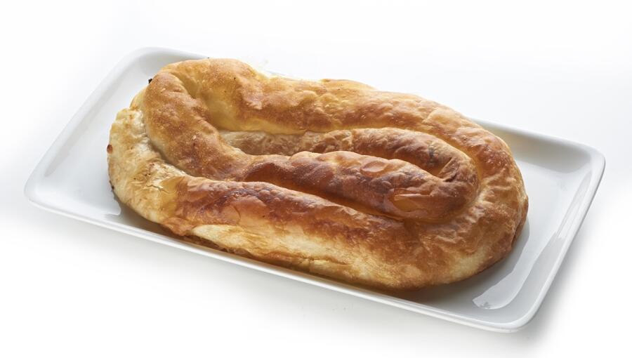 A golden, twisted pastry sits on a white platter, showcasing a flaky and crispy texture.