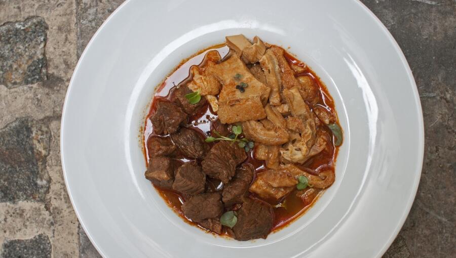 A dish with a rich sauce that includes tender pieces of beef and tripe, garnished with small green herbs.