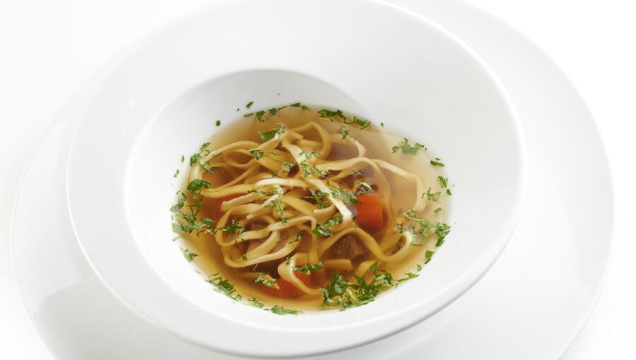 A bowl of clear soup with noodles, herbs and pieces of vegetables.