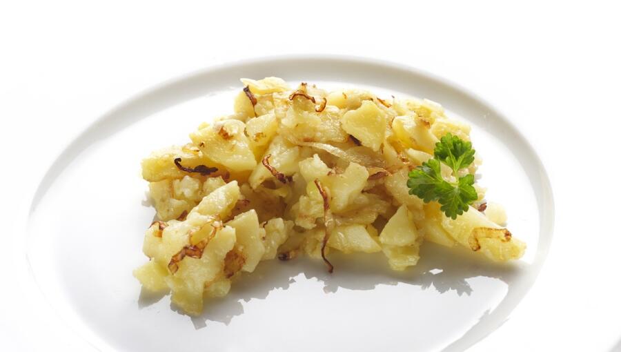 A serving of sautéed potatoes, highlighted with golden edges, rests on a pristine white plate, garnished with a sprig of fresh parsley.