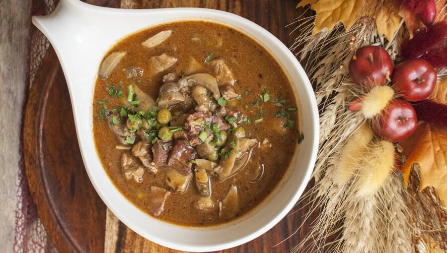 A stew with tender chunks of meat and vegetables in a rich sauce, garnished with fresh herbs, served in a white bowl.