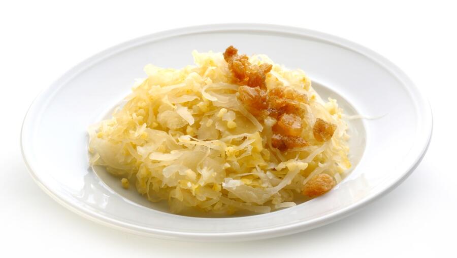 On the white plate, there is a portion of sour cabbage, finely chopped and sprinkled with crunchy pieces.