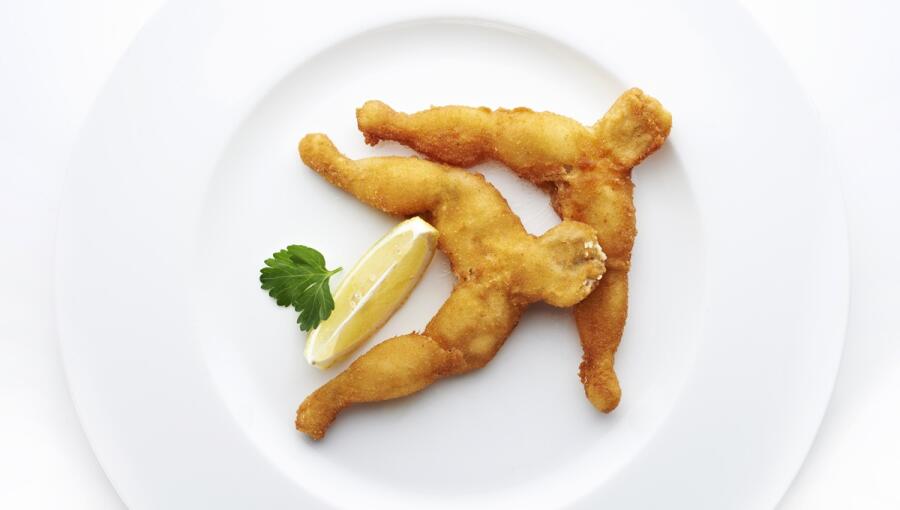 On a white plate, there are two fried frog legs, garnished with a slice of lemon and a sprig of parsley.