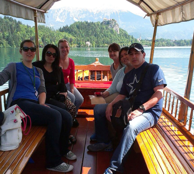 Tourists on a wooden boat on the lake, with a small island in the background.