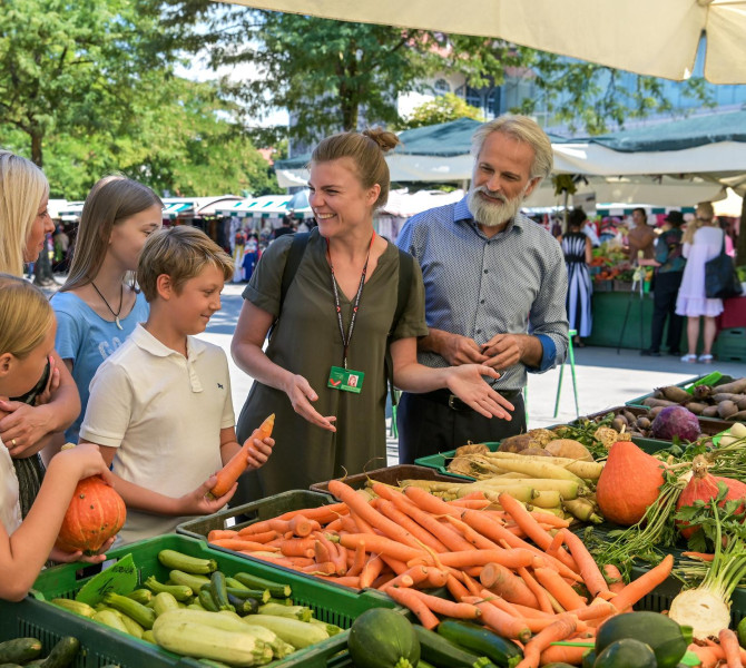 A family with a guide at the market is looking at the vegetable offerings.