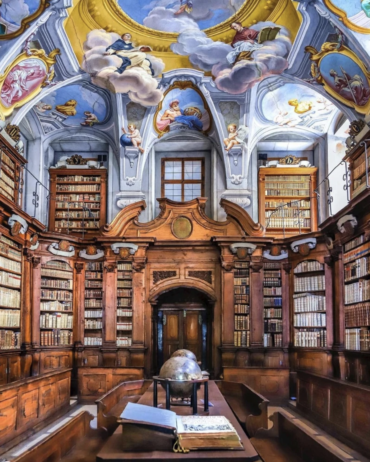 A large library with wooden book shelves. A blue painted ceiling with angels.