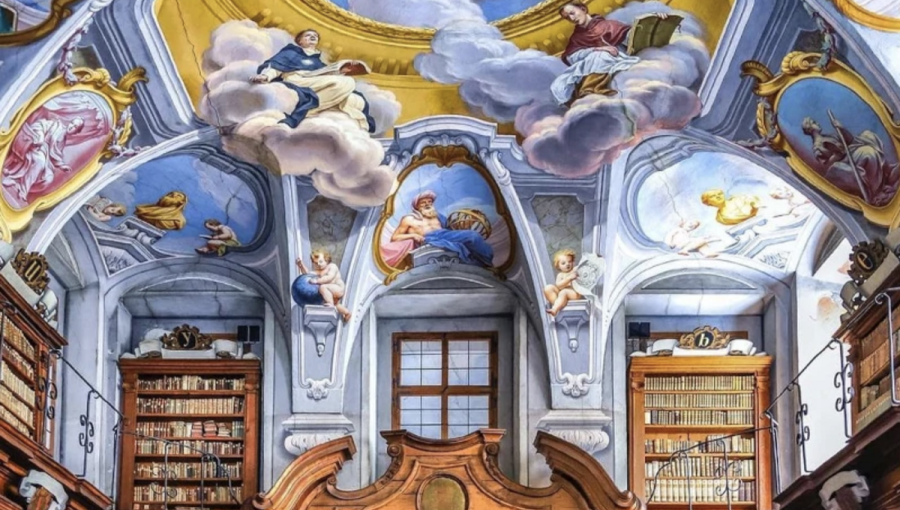 A large library with wooden book shelves. A blue painted ceiling with angels.