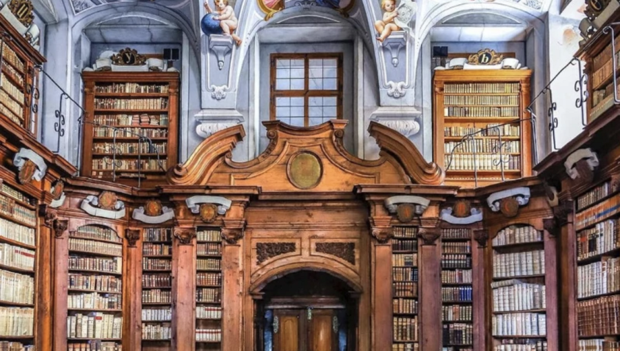A large library with wooden book shelves. A blue painted ceiling with angels.