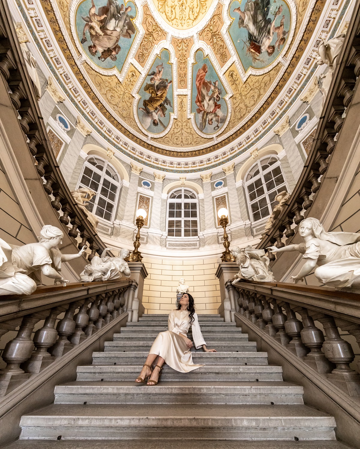 A woman sitting on a staircase. A glorious ceiling above her.