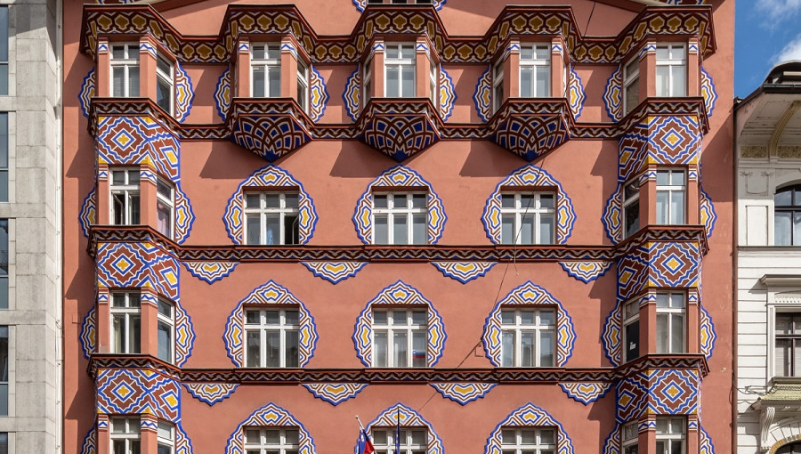 A big dusty pink building with windows adorned with artistic patterns.