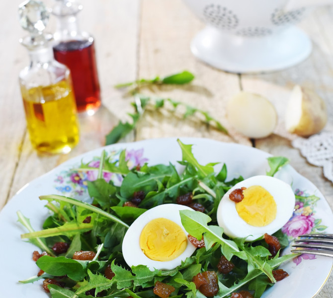Dandelion greens with sliced cooked eggs in a salad on a plate.