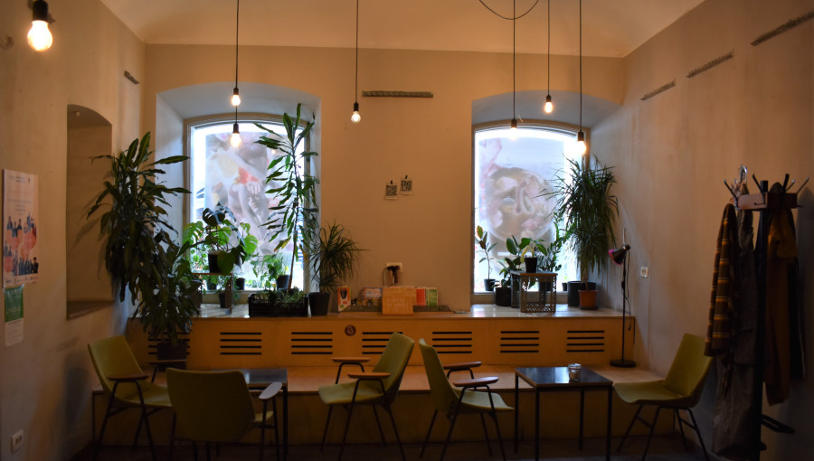 A large room with light walls, two big windows and dark floors. Tables and chairs waiting for guests.